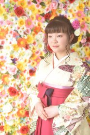 古典柄が入ったクリーム色の着物に赤のグラデーションの袴を着た女の子。花の背景