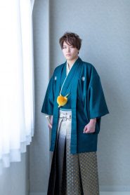 濃い緑色の紋付き羽織袴に、白から黒のグラデーションに金の市松模様入りの袴を着付けられた成人式の前撮り写真