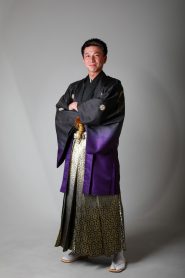 黒から紫のぼかし入り羽織に黒の着物、白から黒の金柄袴を着た成人式を迎える男子の立姿