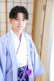 羽織は藤色、中の着物は白、袴は紫の紋付き袴を着用した二十歳の集いに参加する成人者の男性。前撮りで撮影された写真