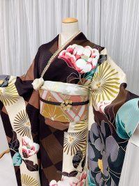 焦げ茶に大きな椿が描かれたかわいいにピンクの幾何学模様帯を合わせた振袖コーデ